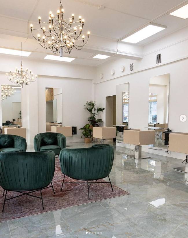 Kadeřnický salon osvětlený velkými lustry a panelovými světly.
